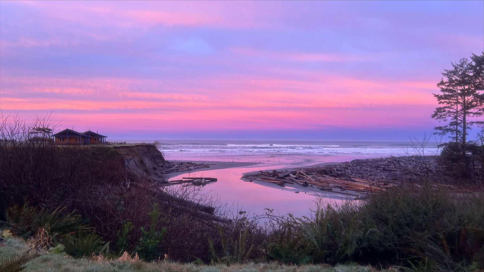 Pink and purple sunset over Kalaloch Beach in Olympic National Park, with driftwood, a tidal creek and bluff-top cabins