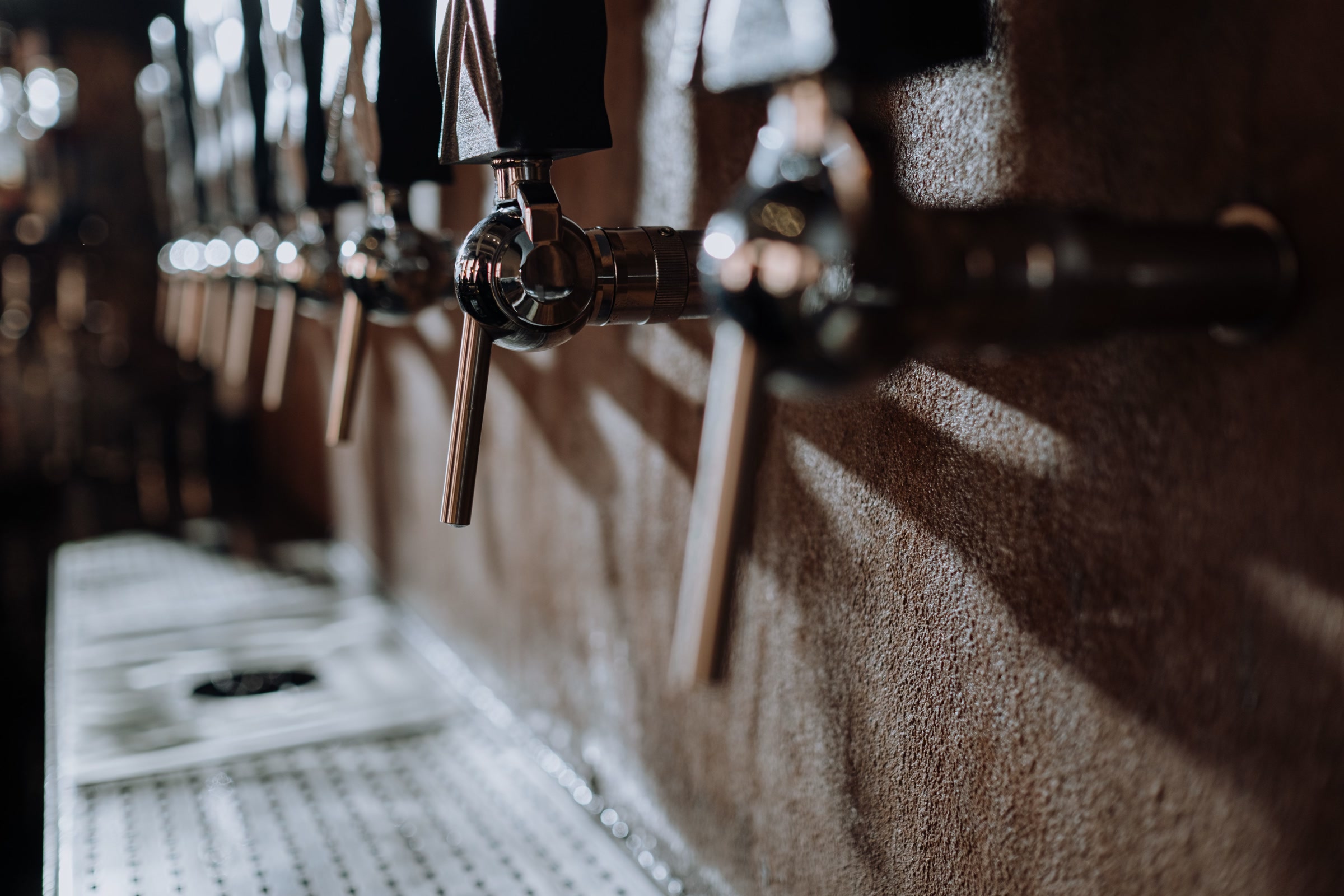 Close-up of a row of metal beer taps in a dim, warmly lit bar