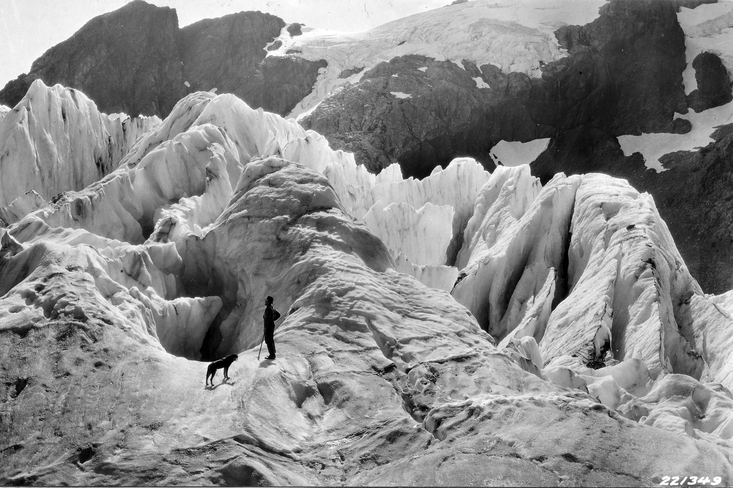 Black and white 1927 photo of a person and a dog standing among tall ice ridges and crevasses on the Blue Glacier