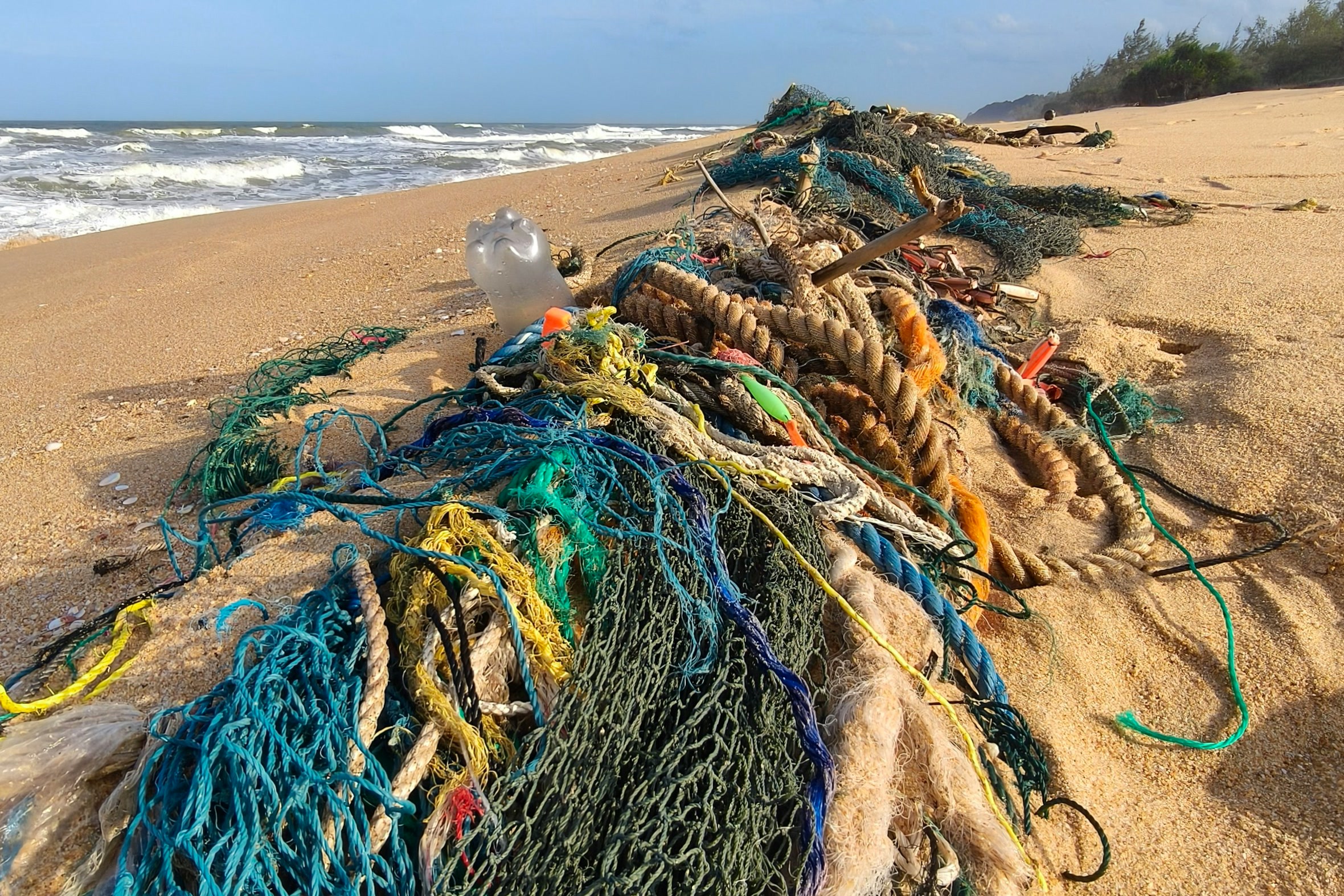 Tangled lost fishing nets, rope and a plastic bottle washed up along a sandy ocean beach