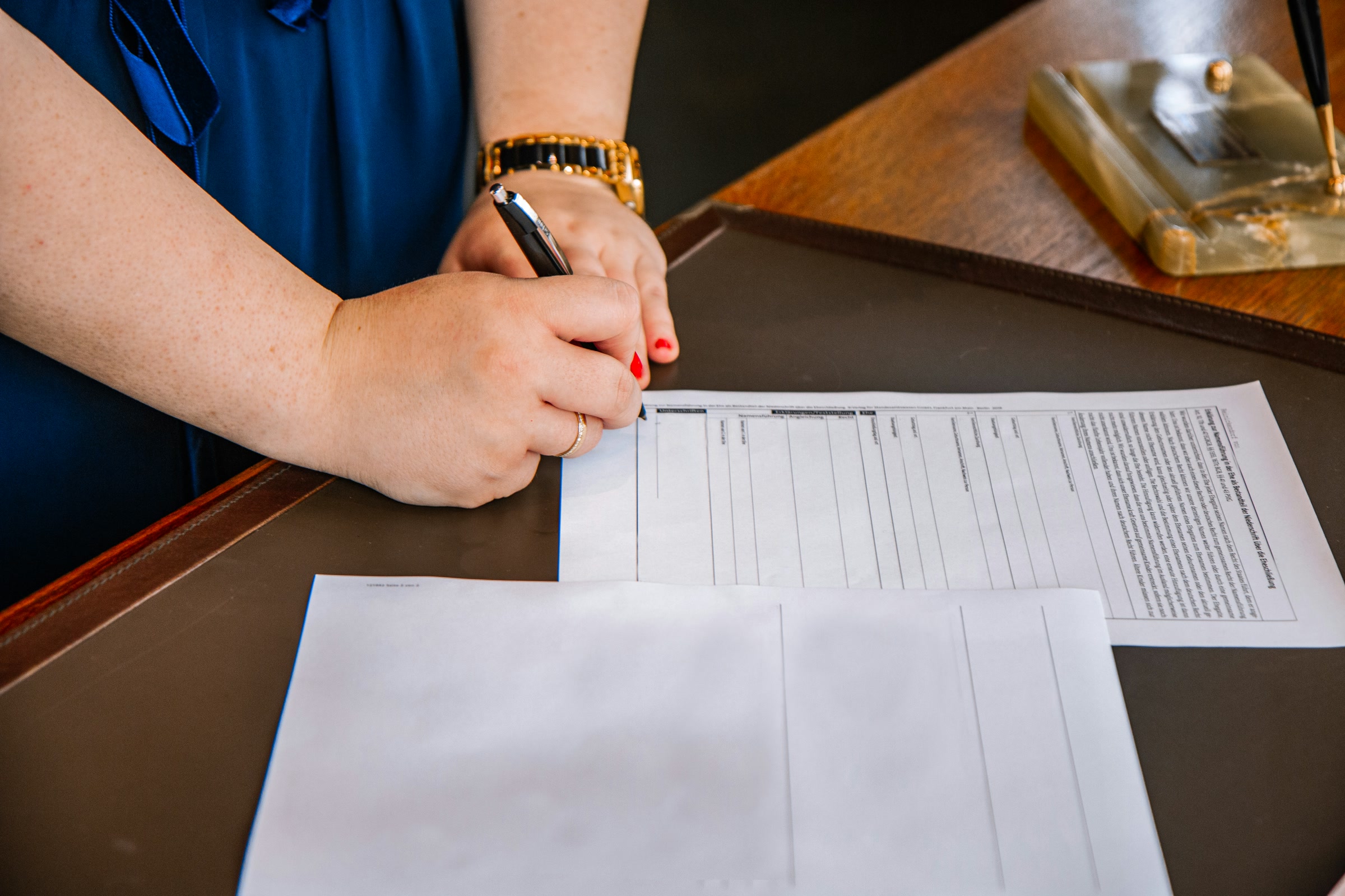 Hands holding a pen fill in a printed form on a dark wooden desk, face not shown