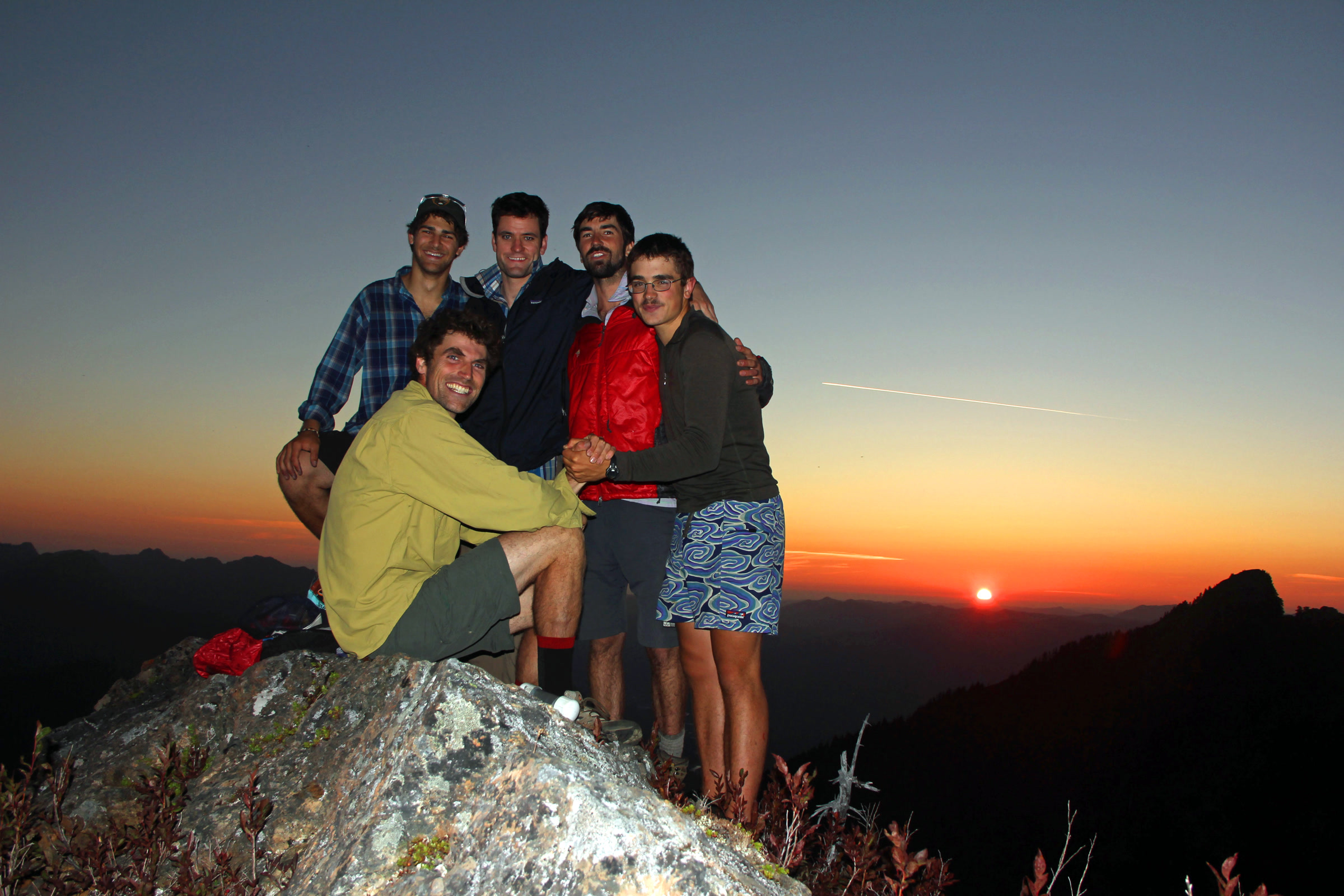 A group of five hikers gathered on a rocky ridge as the sun sets over the Olympic Mountains