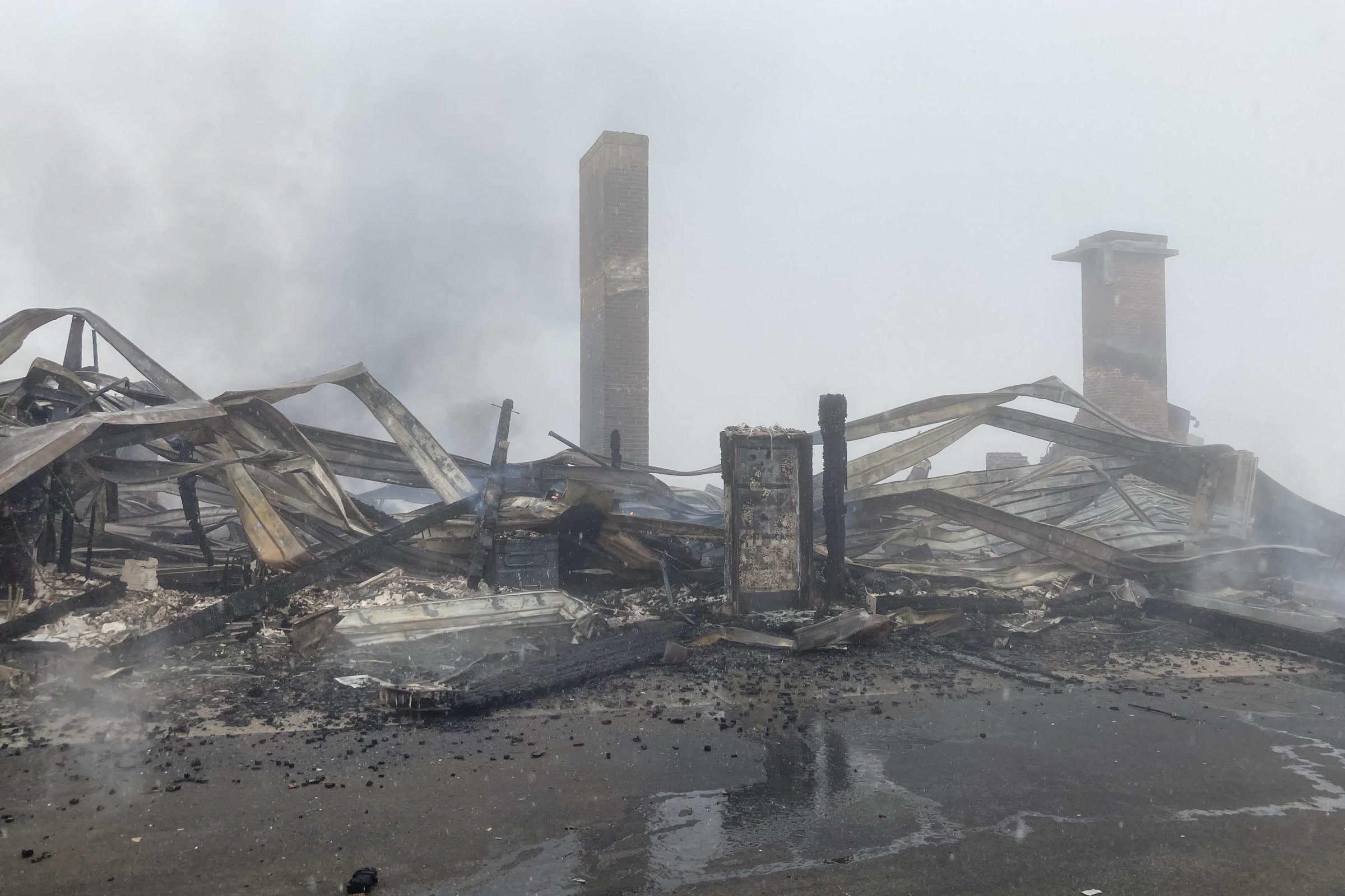 Smoking wreckage of the Hurricane Ridge Day Lodge, with twisted metal roofing and two stone chimneys still standing in fog