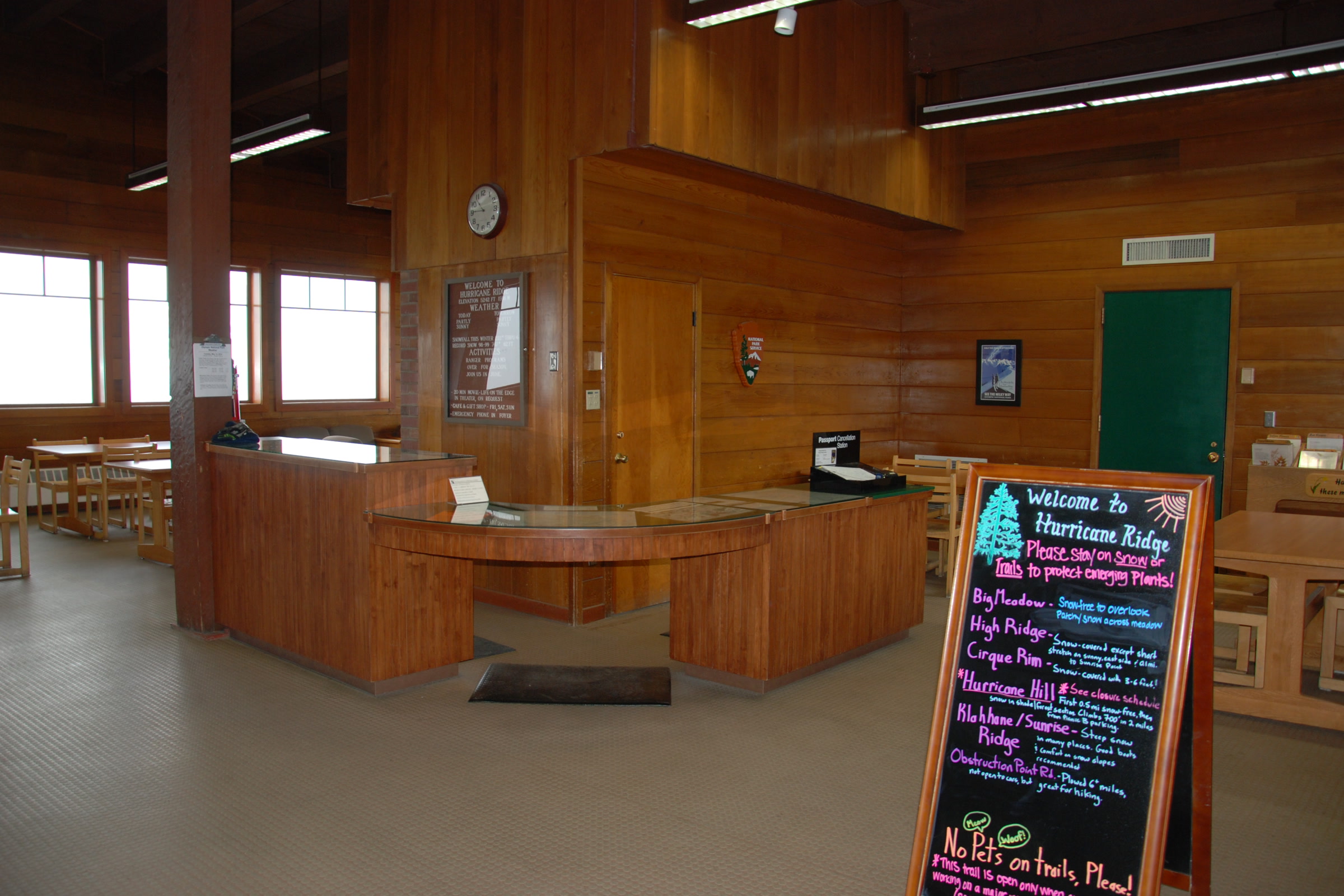Wood-panelled interior of the Hurricane Ridge Day Lodge with a curved information desk, tables and a chalkboard of trail conditions