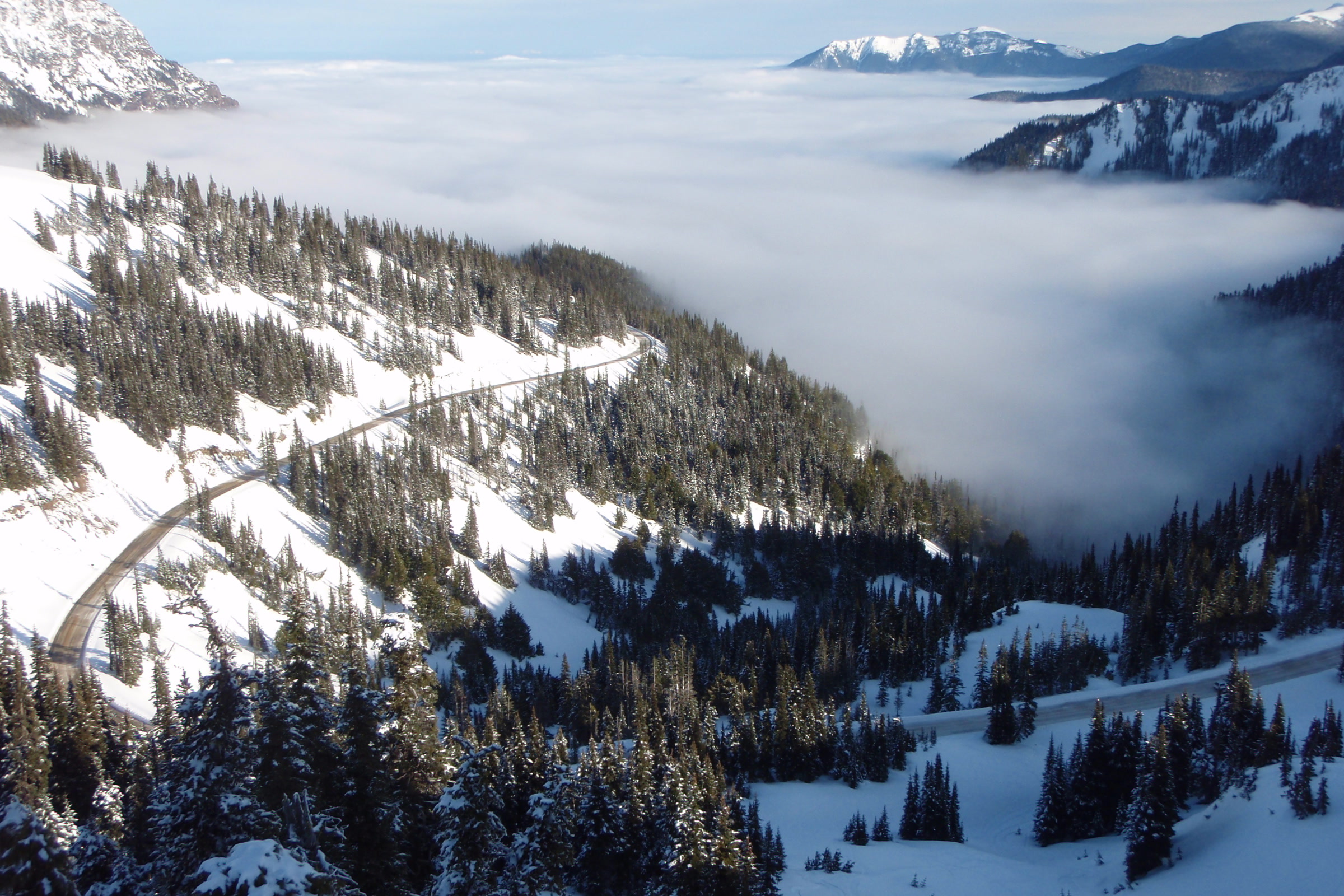 Hurricane Ridge Road winding across snowy forested slopes above a valley filled with cloud