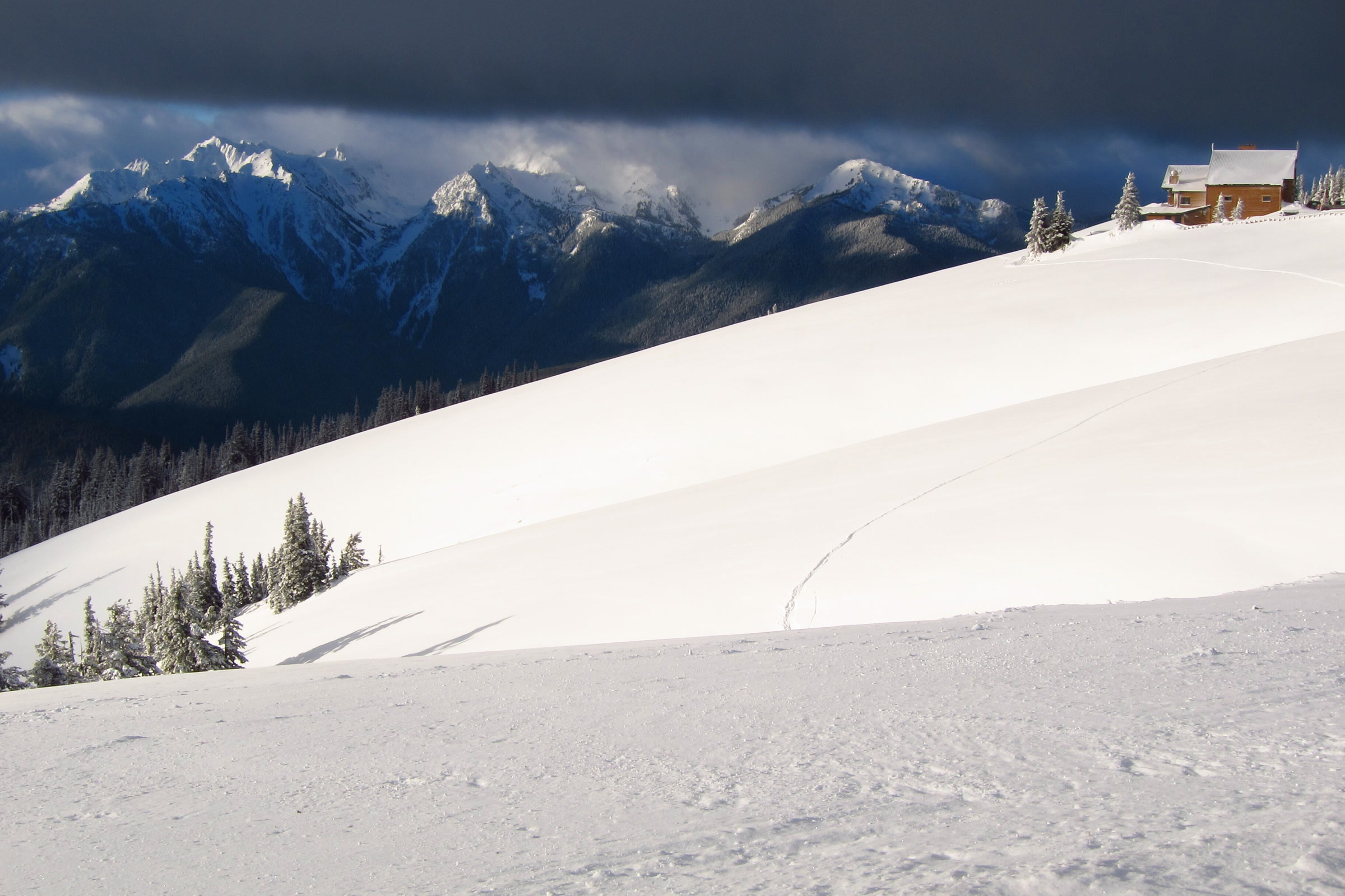Hurricane Ridge Visitor Center on a deep snowfield below snow-covered Olympic peaks and dark winter clouds