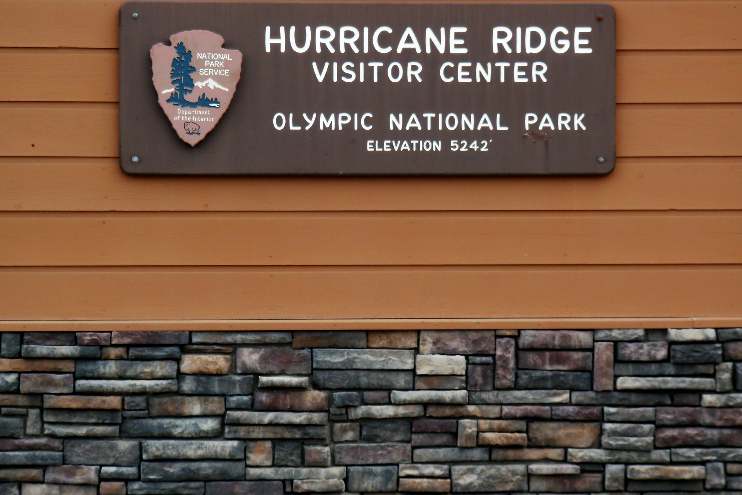 Brown National Park Service sign with the arrowhead emblem reading Hurricane Ridge Visitor Center, Olympic National Park, elevation 5242 feet