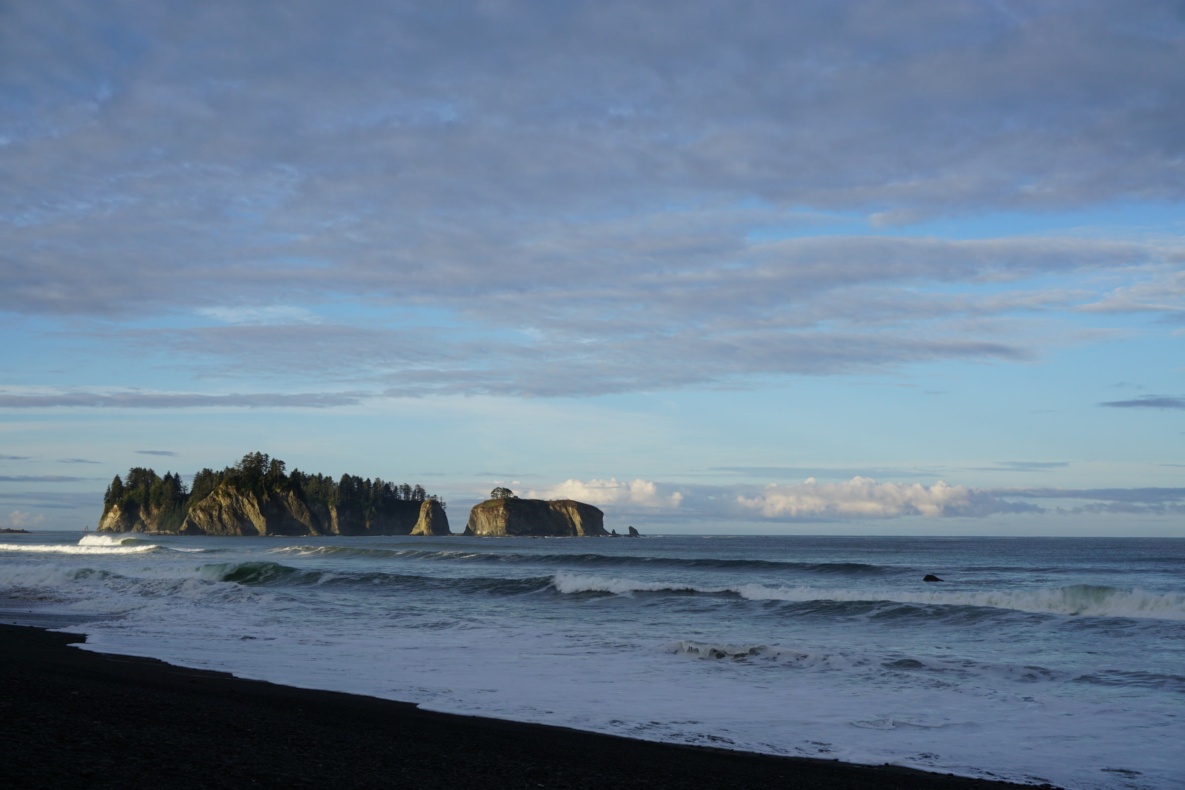 Forested James Island off the mouth of the Quillayute River, seen across the surf from Rialto Beach on a clear summer morning