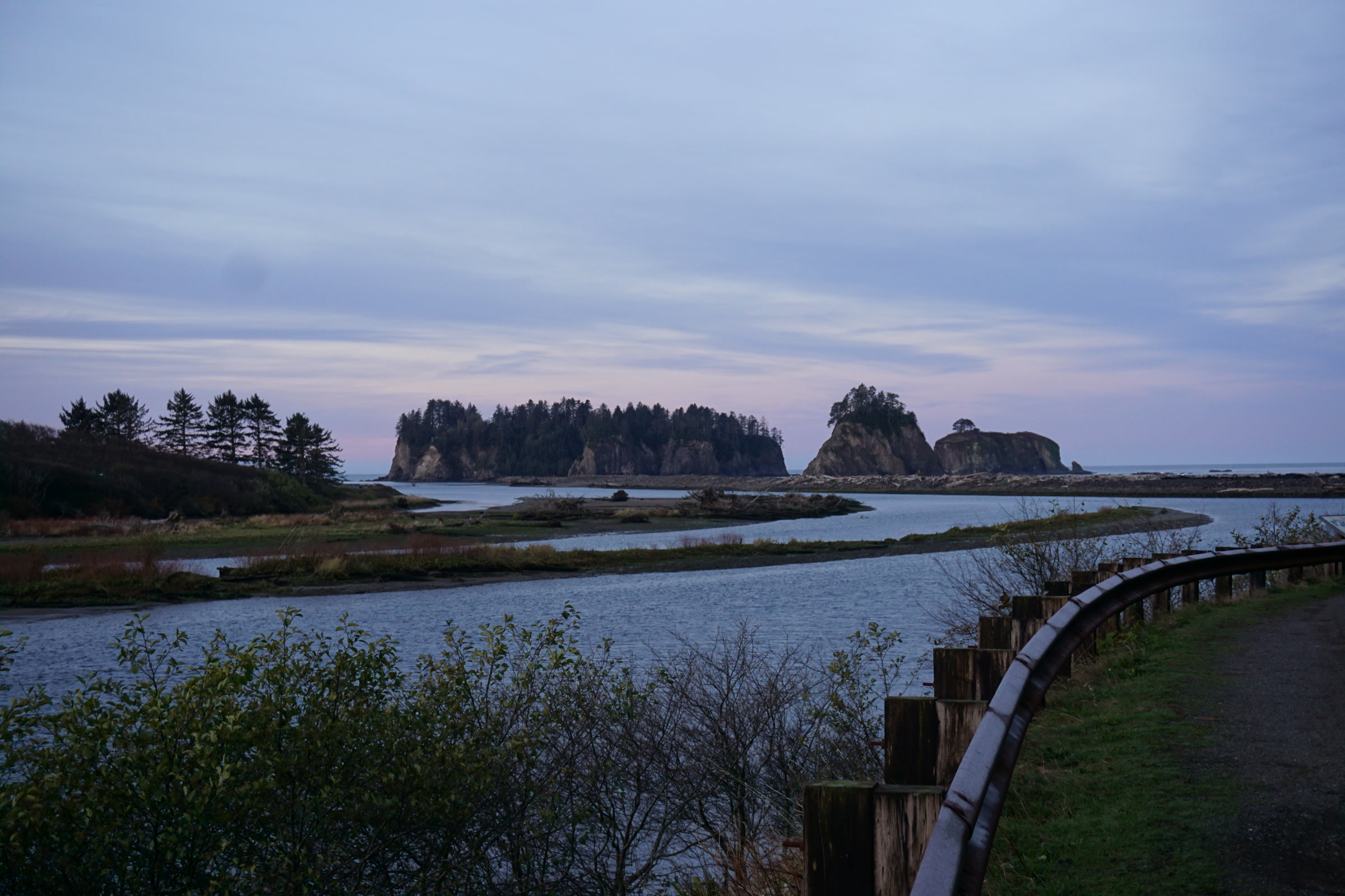 Soft pink dawn light over the mouth of the Quillayute River, with the forested sea stack of James Island offshore