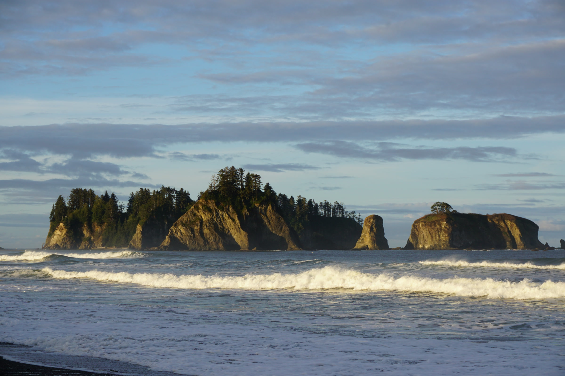 James Island and neighboring forested sea stacks lit by evening sun beyond breaking surf off the Olympic coast near La Push