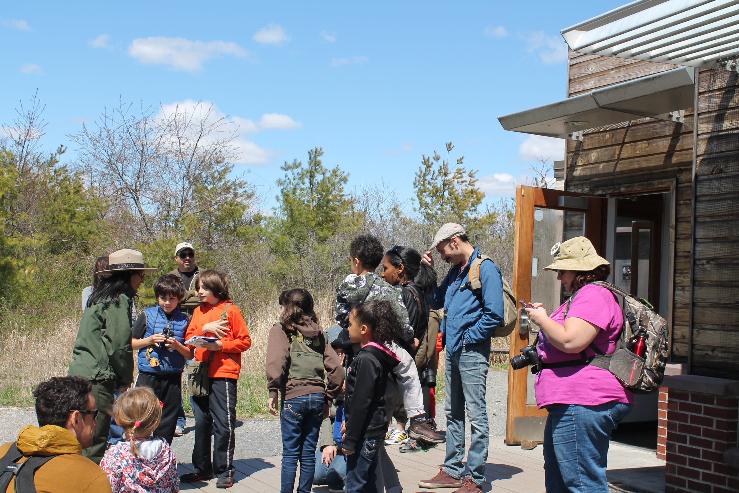 Rangers, children and parents gathering outside a visitor center for a Junior Ranger Day nature hike
