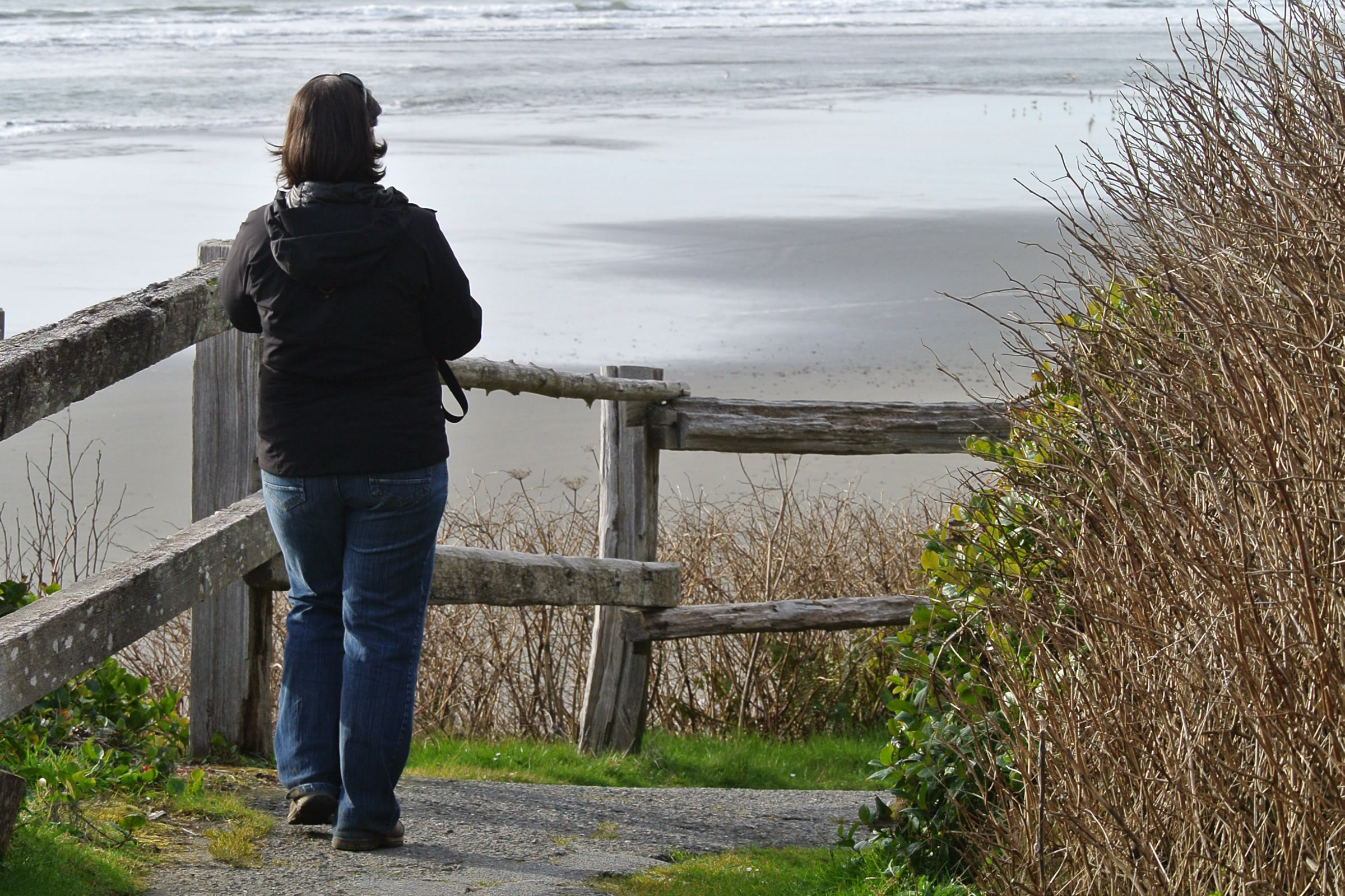 A visitor seen from behind at a weathered wooden railing where the beach access path from Kalaloch Campground meets the sand