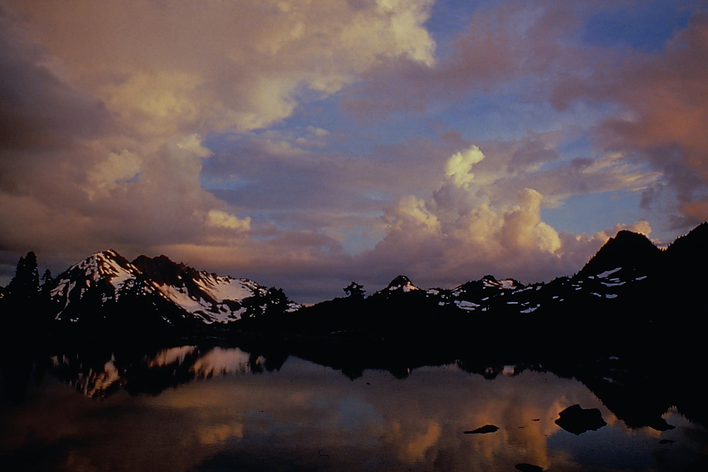 Snow-streaked peaks and glowing evening clouds reflected in a calm mountain lake in LaCrosse Basin