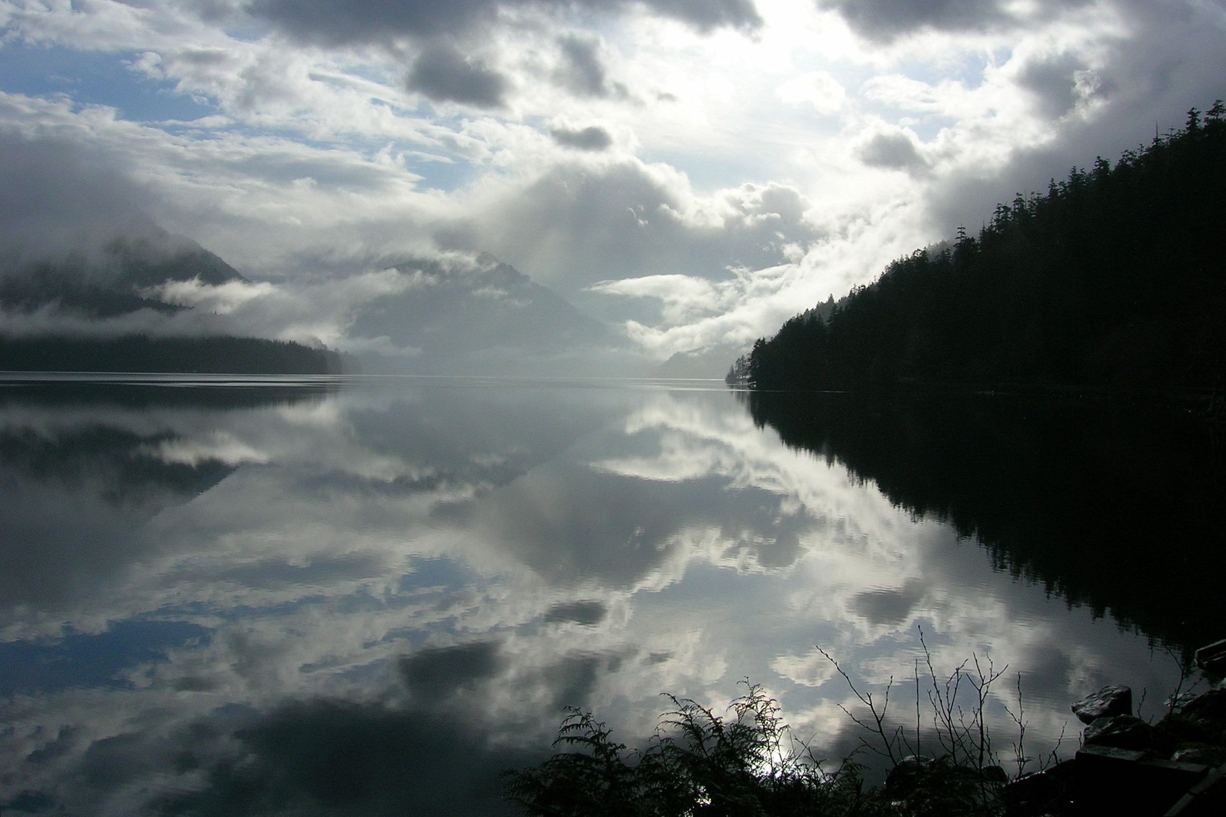 Still water of Lake Crescent mirroring bright clouds between forested hillsides