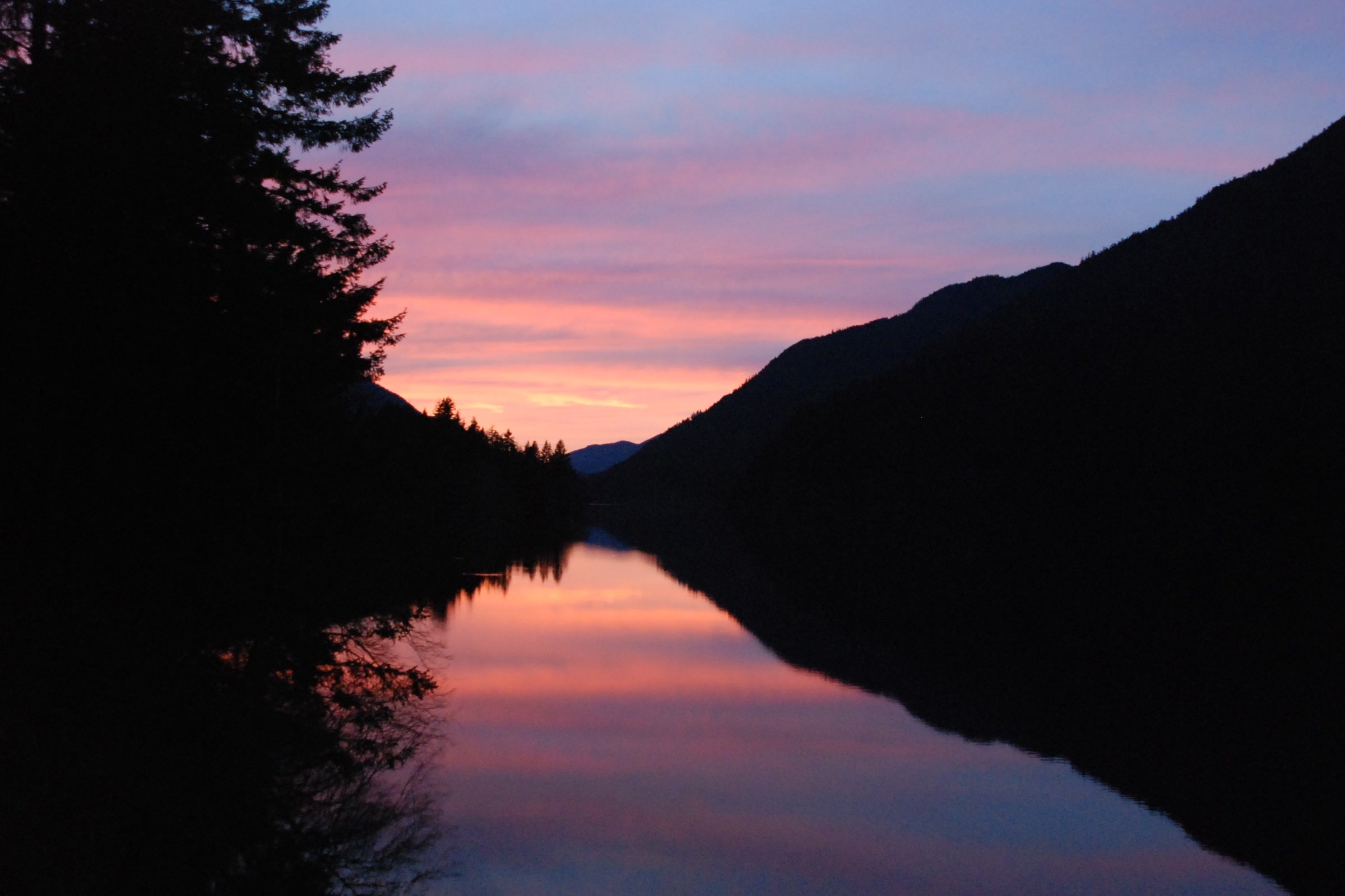 Pink and purple sunset sky mirrored in the still water of Lake Crescent between dark forested slopes