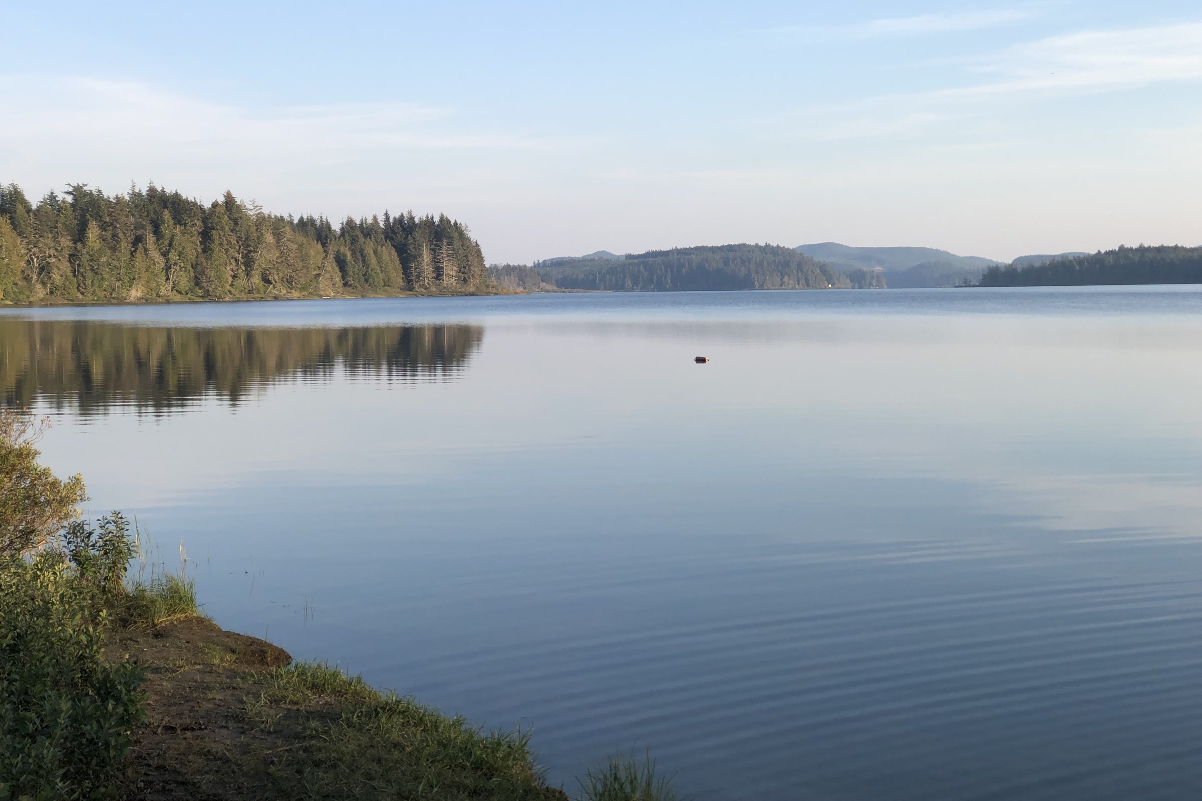 Glassy Lake Ozette at dusk, seen from the campground shore, with low forested hills and a pale sky reflected in the water