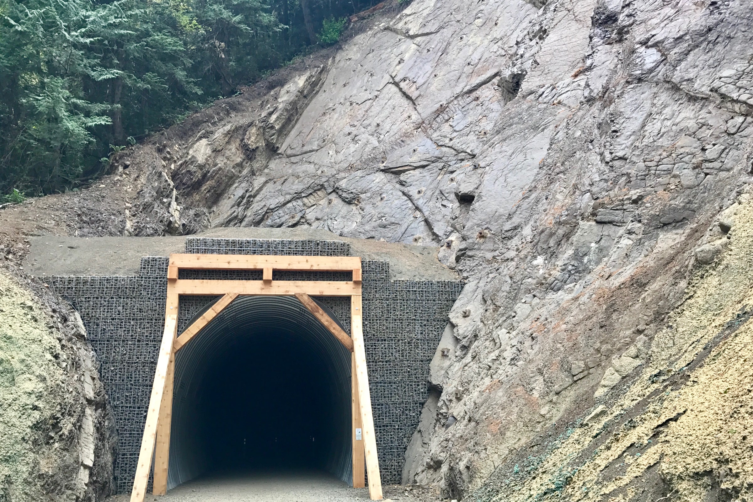 The timber framed entrance of the restored McFee Tunnel cut into grey rock on the Spruce Railroad Trail
