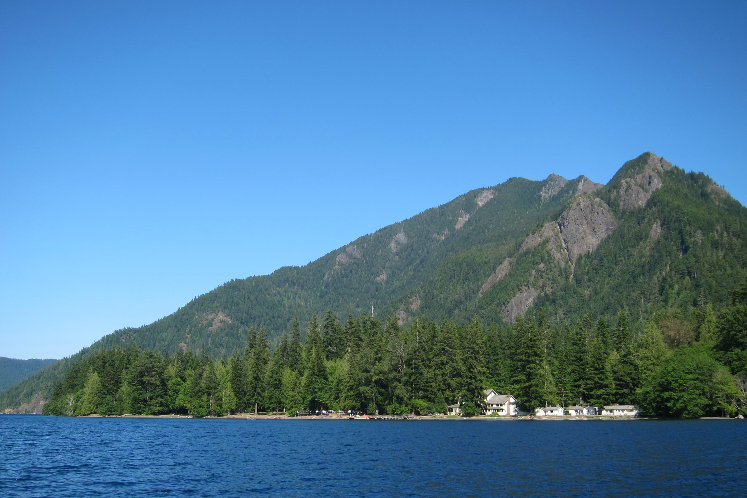 Mount Storm King rising steep and forested above the deep blue water of Lake Crescent, with buildings along the lakeshore below