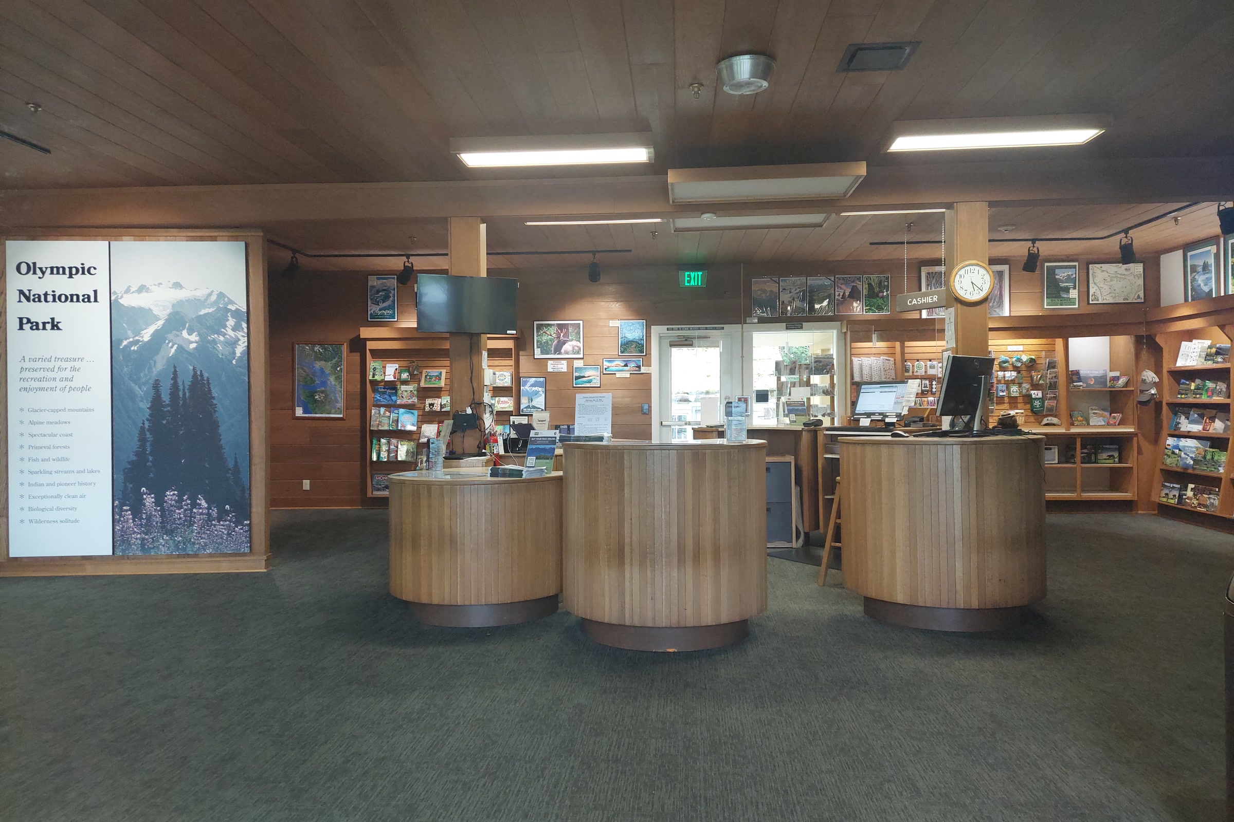 Round wooden information desks, bookshelves and a tall Olympic National Park mountain panel inside the visitor center lobby in Port Angeles