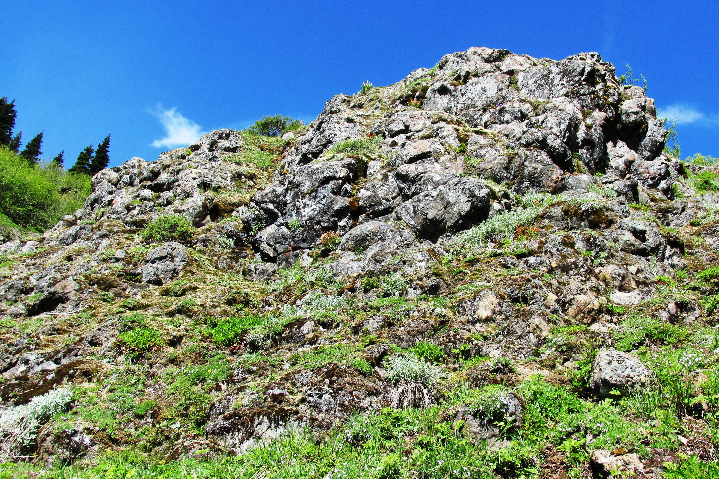 A craggy outcrop of dark, rounded basalt pillows rising above a green slope under a deep blue sky