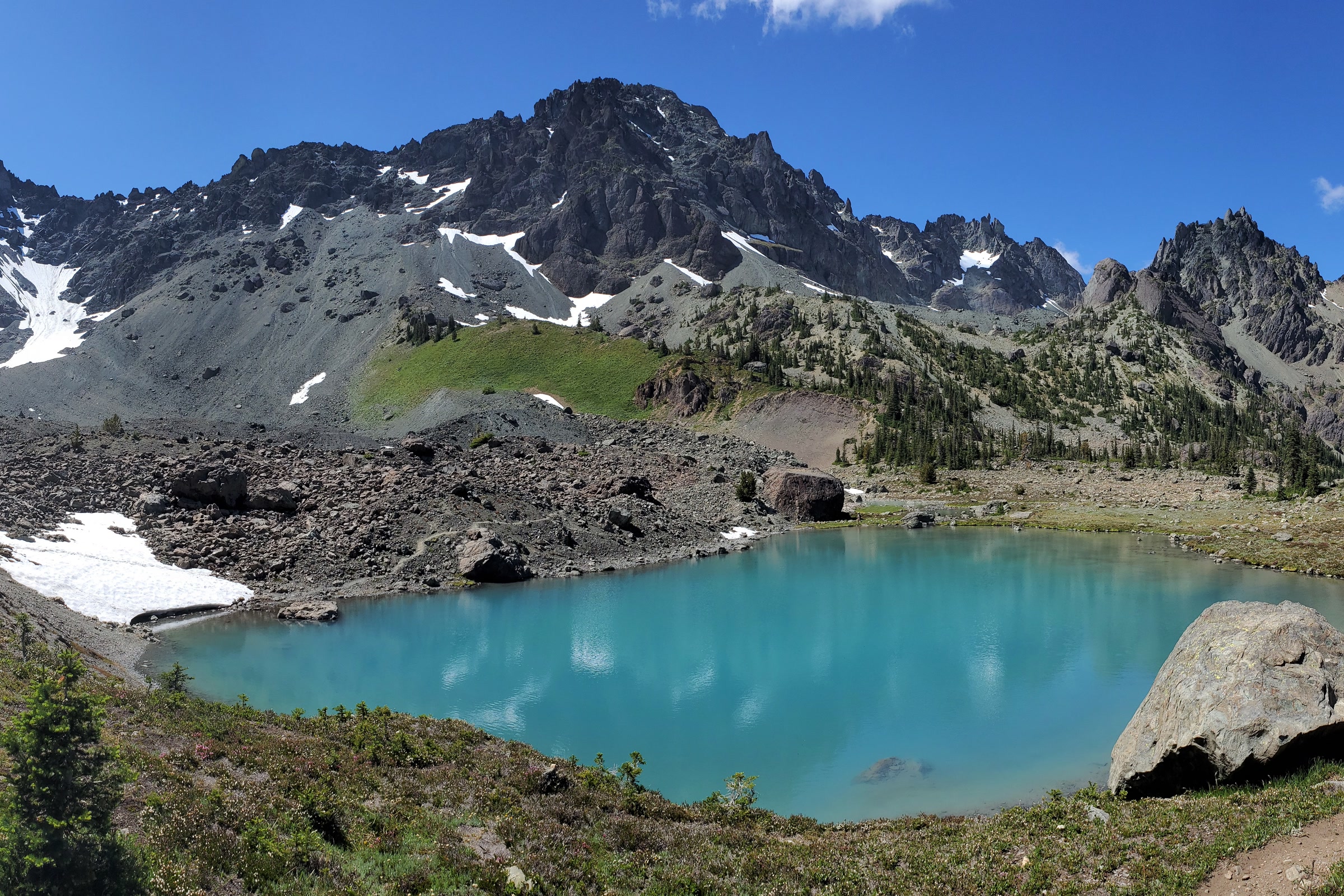A turquoise tarn in rocky Royal Basin below the jagged, snow-patched face of Martin Peak in the Olympic Mountains