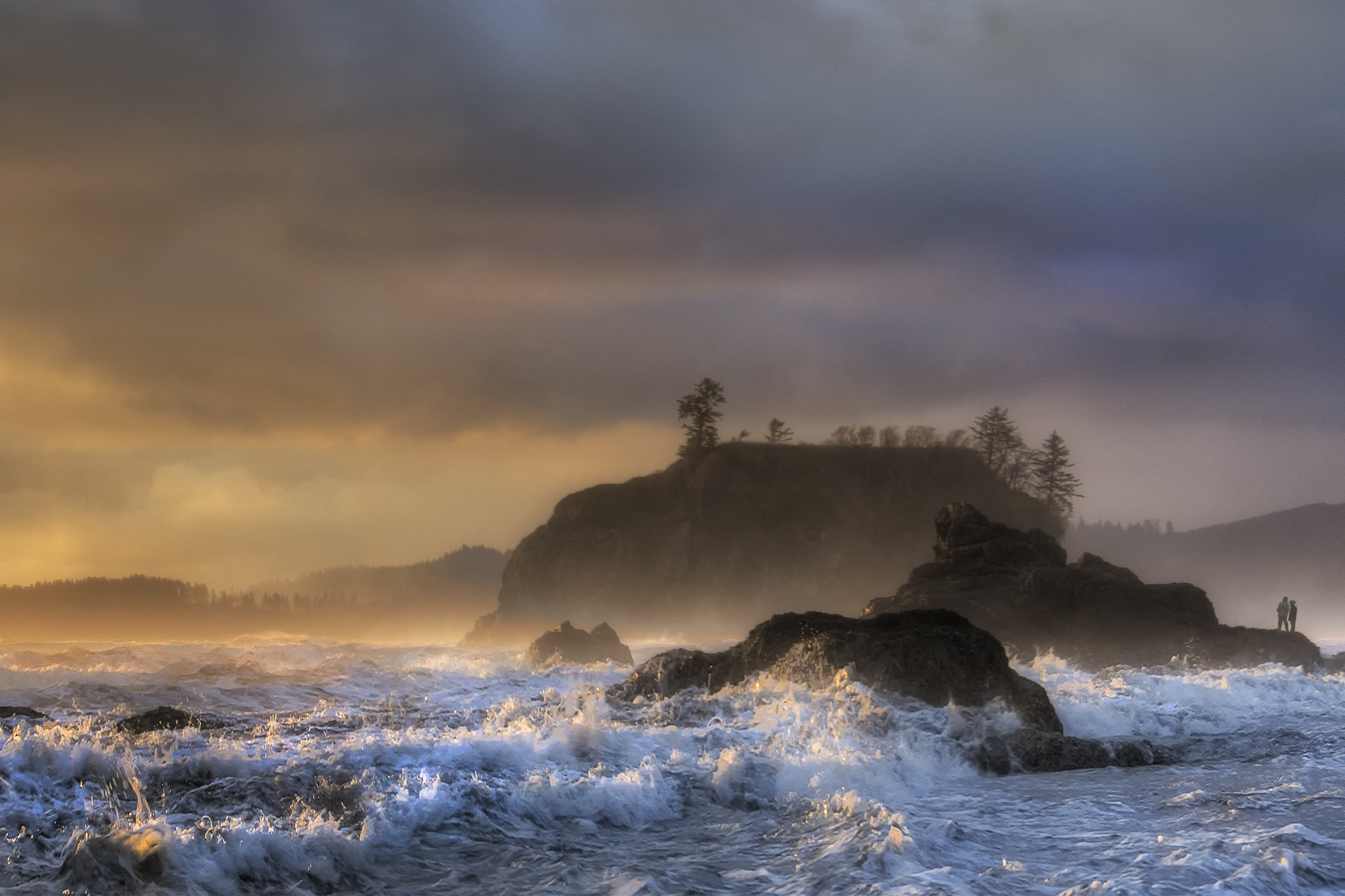 Storm surf foaming around rocks at the north end of Ruby Beach under dark clouds lit gold by a low sun