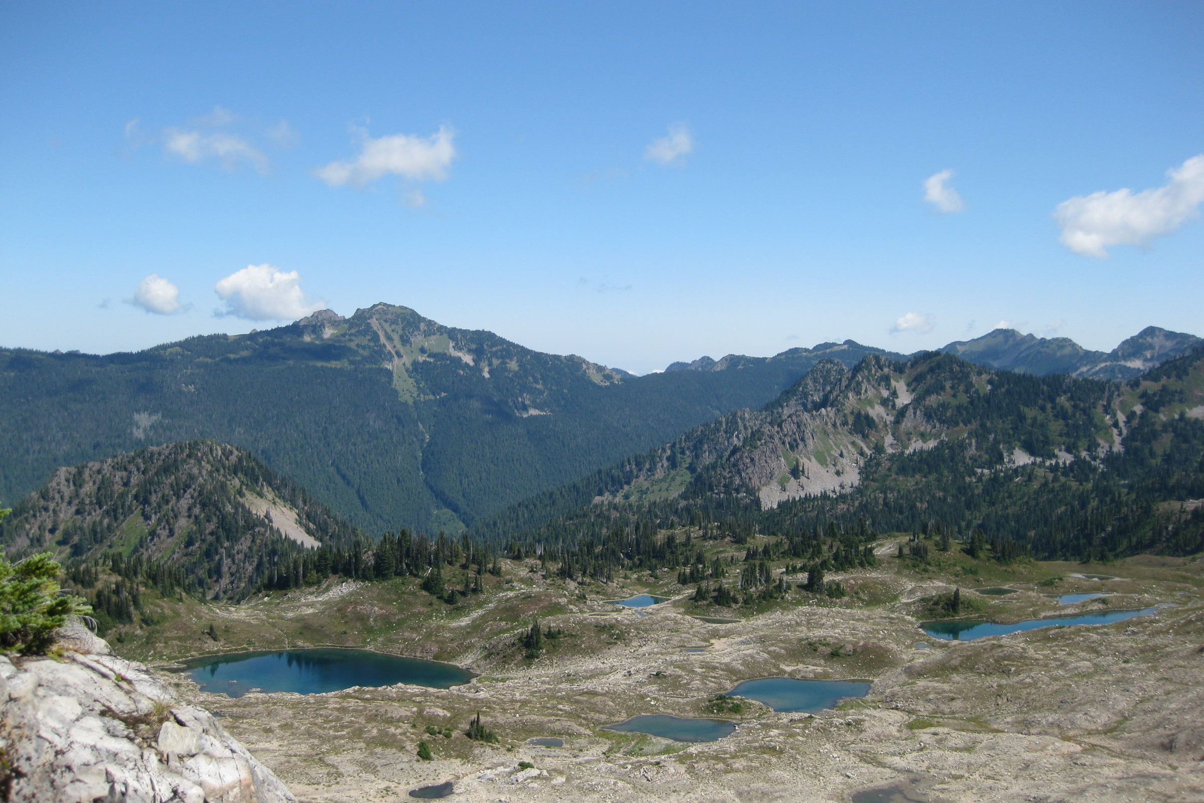 Small blue lakes scattered across the rocky Seven Lakes Basin, seen from the High Divide Trail with mountains behind