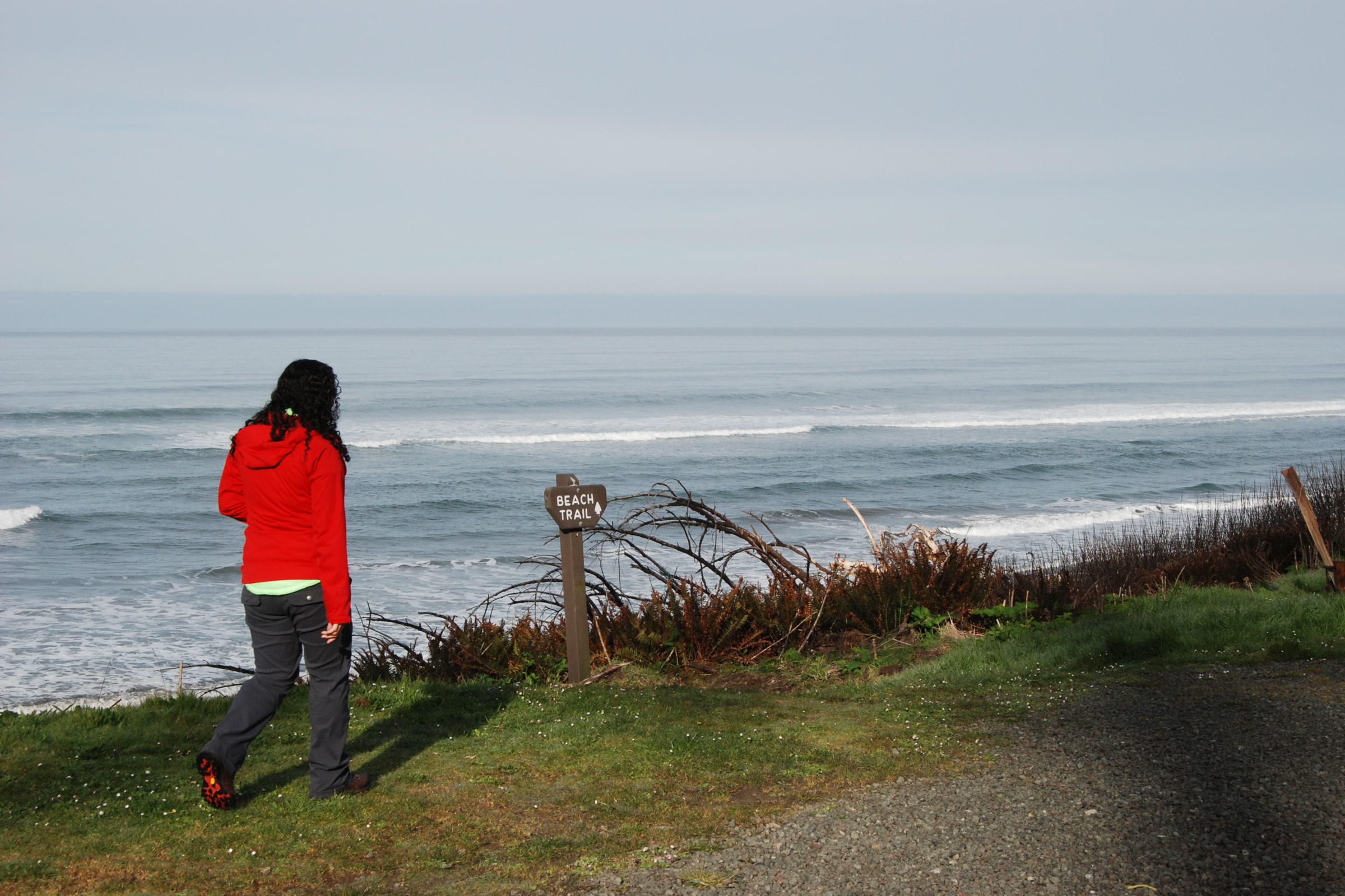 A visitor in a red jacket walking along the grassy bluff at South Beach Campground above Pacific surf