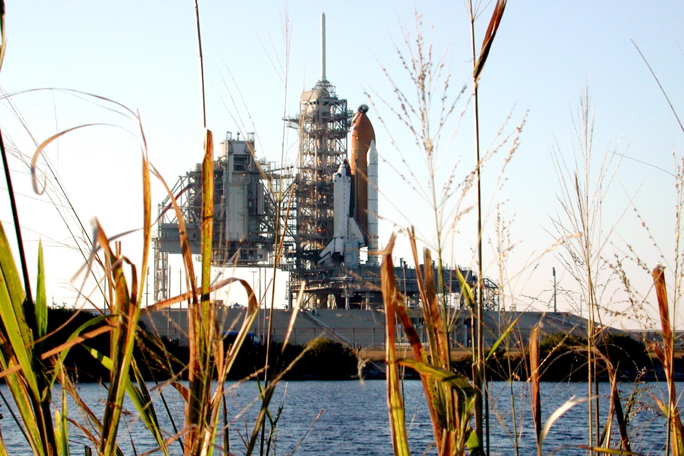 Space Shuttle Columbia on Launch Pad 39A at Kennedy Space Center, seen across the water through tall marsh grasses before the STS-107 launch