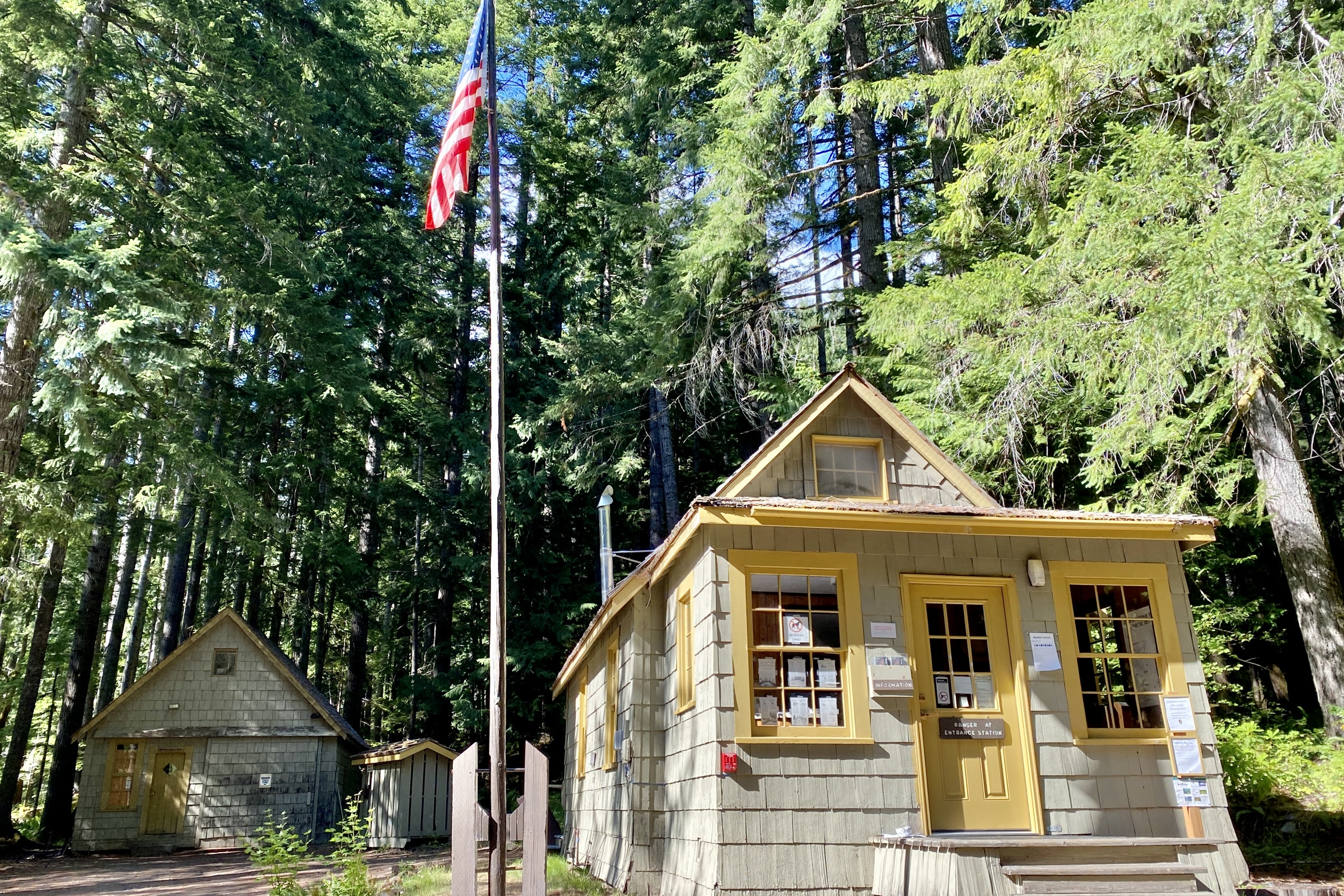 The small wooden Staircase Ranger Station with yellow trim and a flagpole among tall trees in Olympic National Park