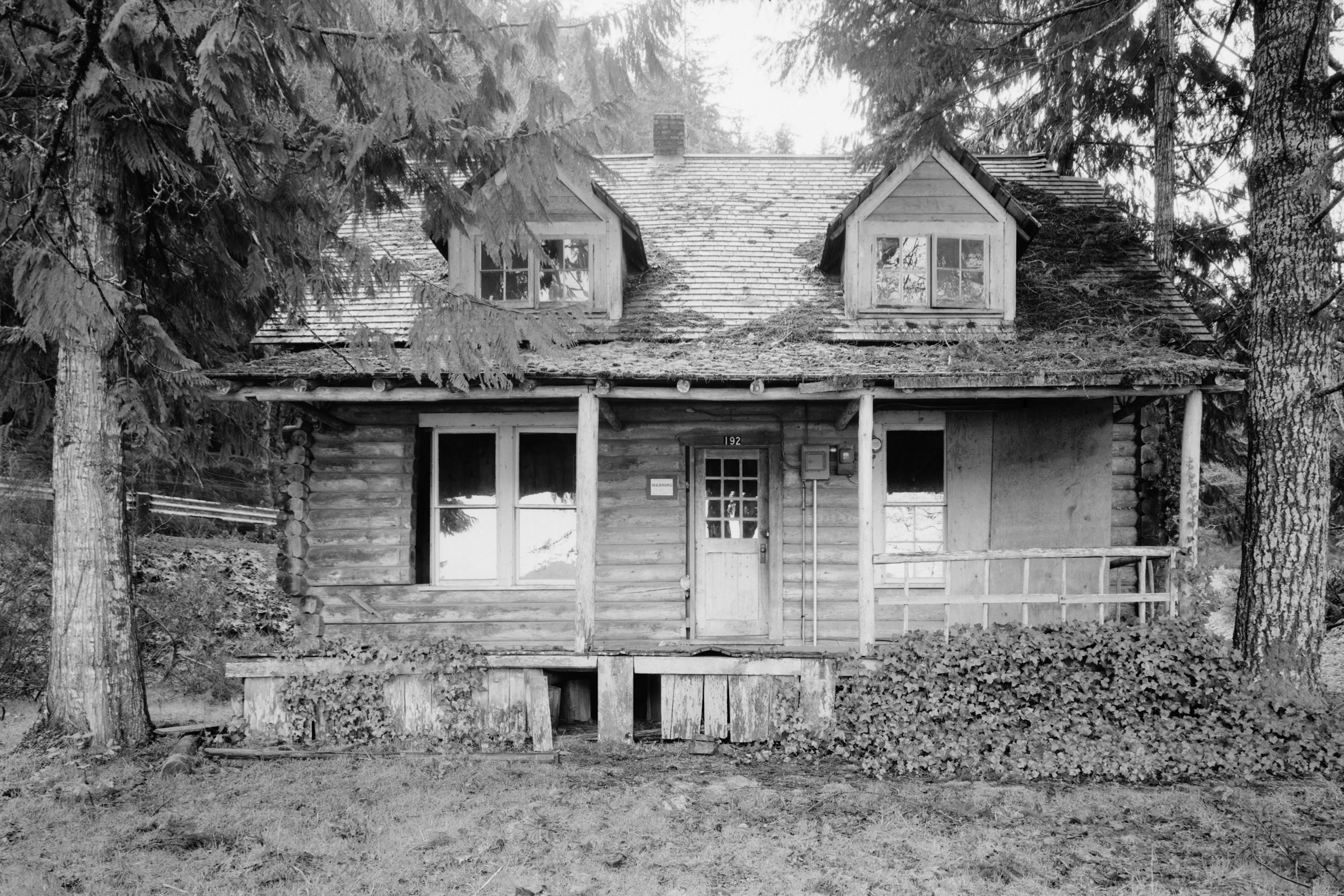 Black-and-white 1983 survey photo of Storm King Ranger Station, a log cabin with twin dormers and a sagging front porch among conifers
