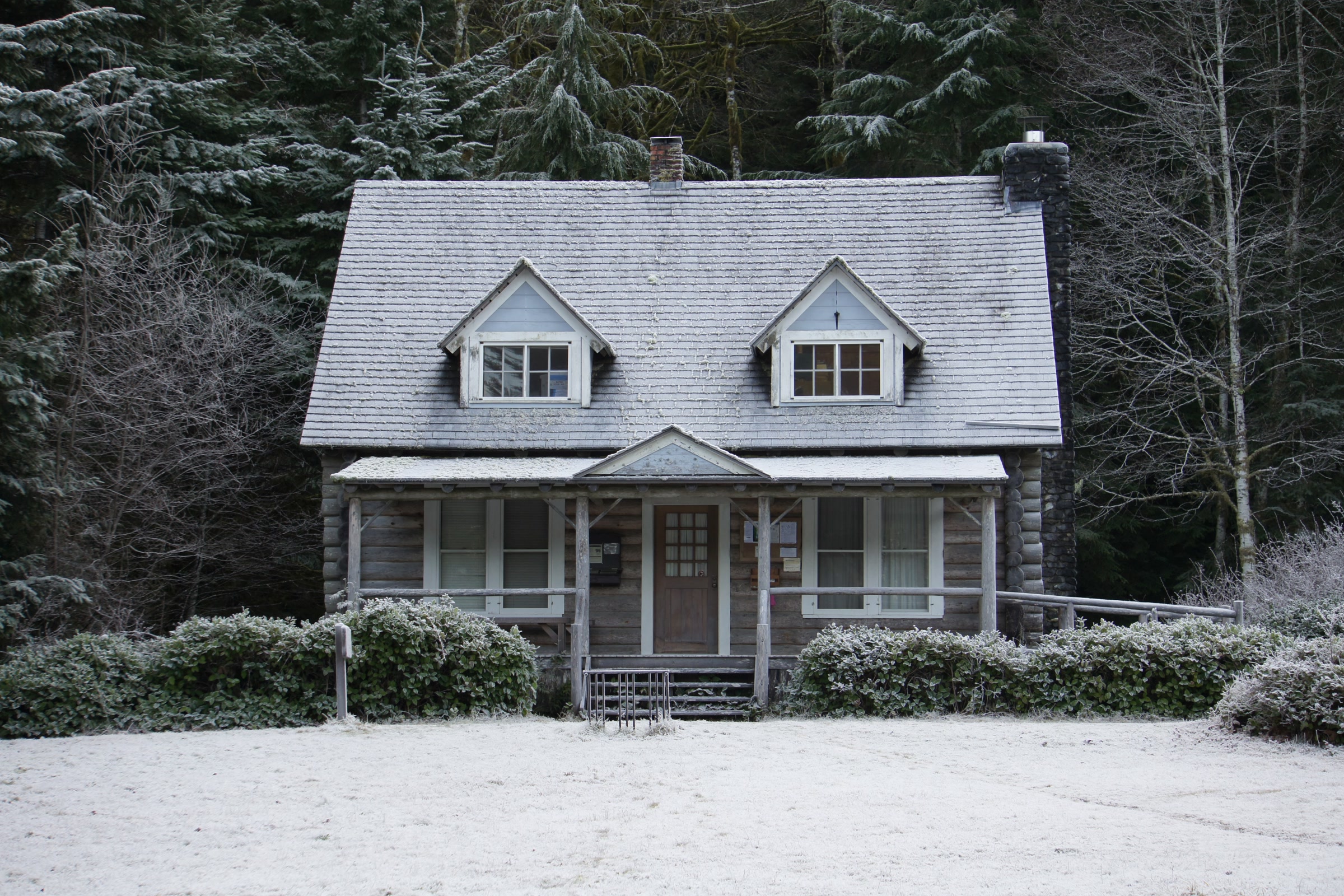 Storm King Ranger Station, a log cabin with twin dormers, under a light dusting of snow in front of dark winter forest at Lake Crescent