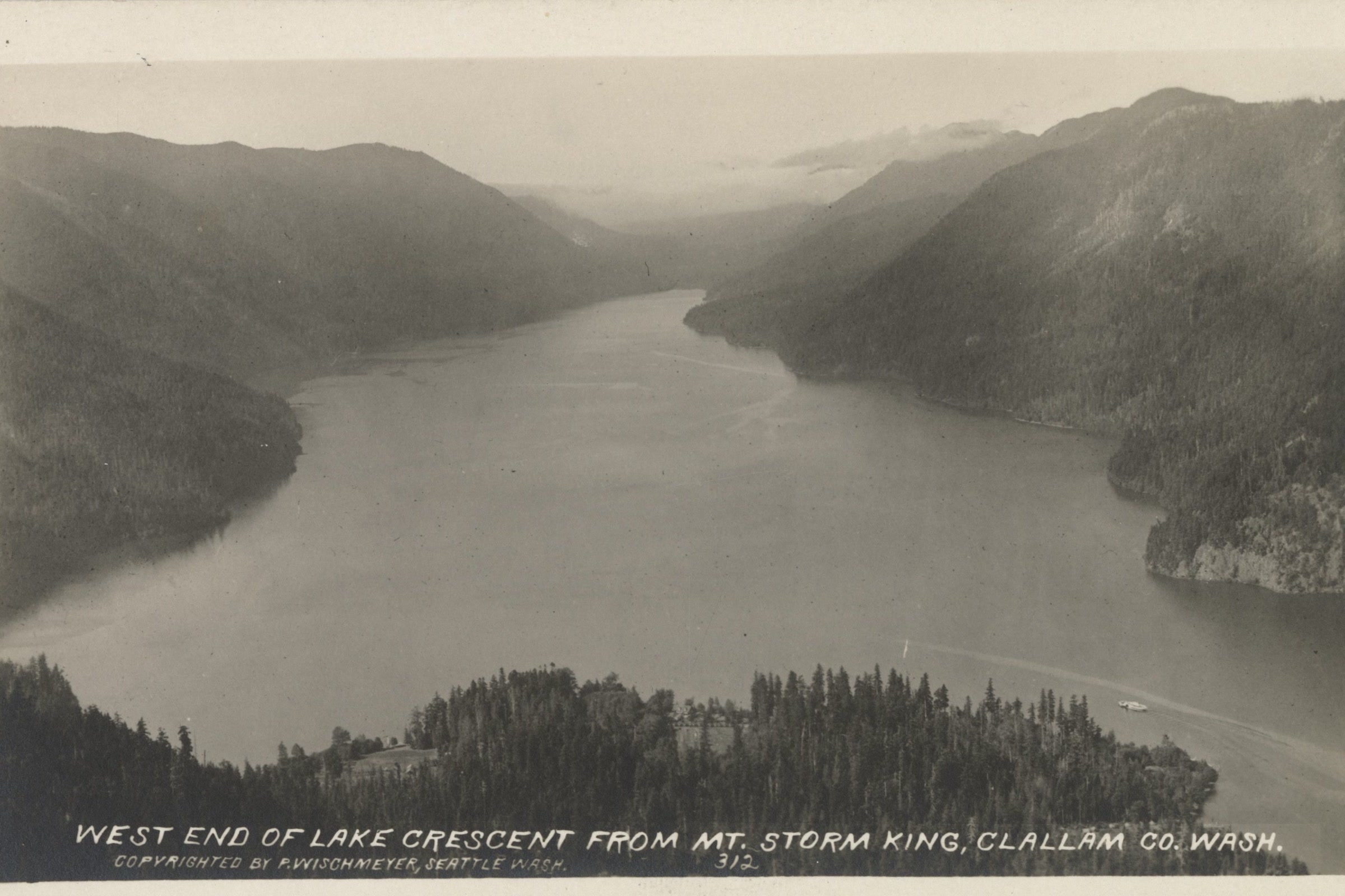 Black and white postcard view from Mount Storm King down the length of Lake Crescent to its west end, between steep forested ridges